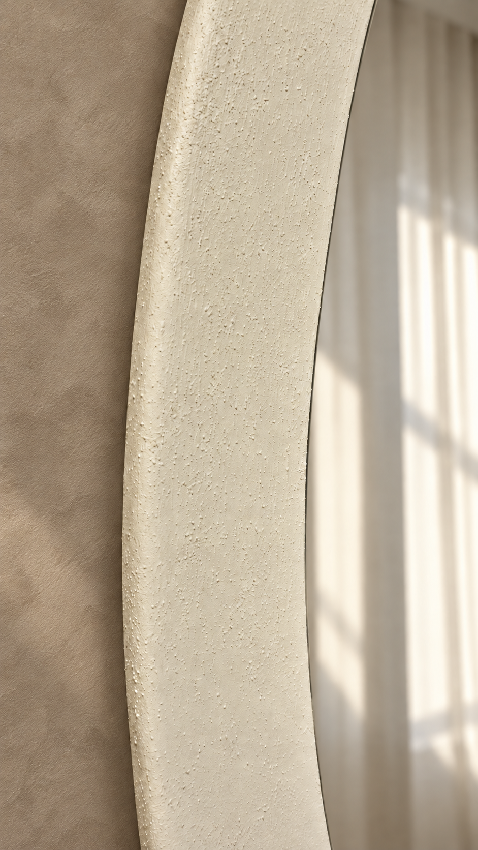 Close-up of a textured, curved cream-colored frame or trim against a warm beige wall with soft window light casting shadows.