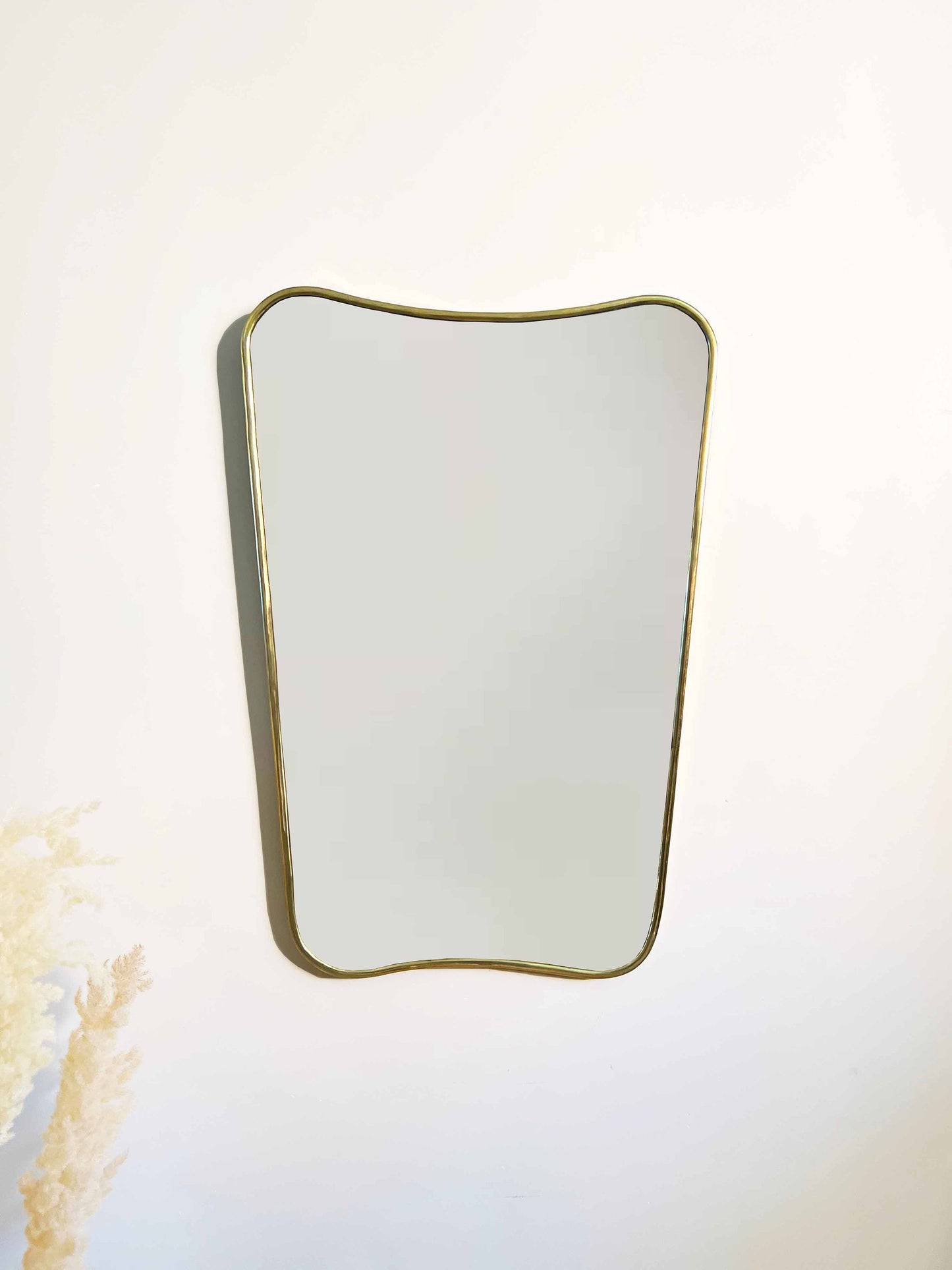 a white wall with a brass mirror hanging on it