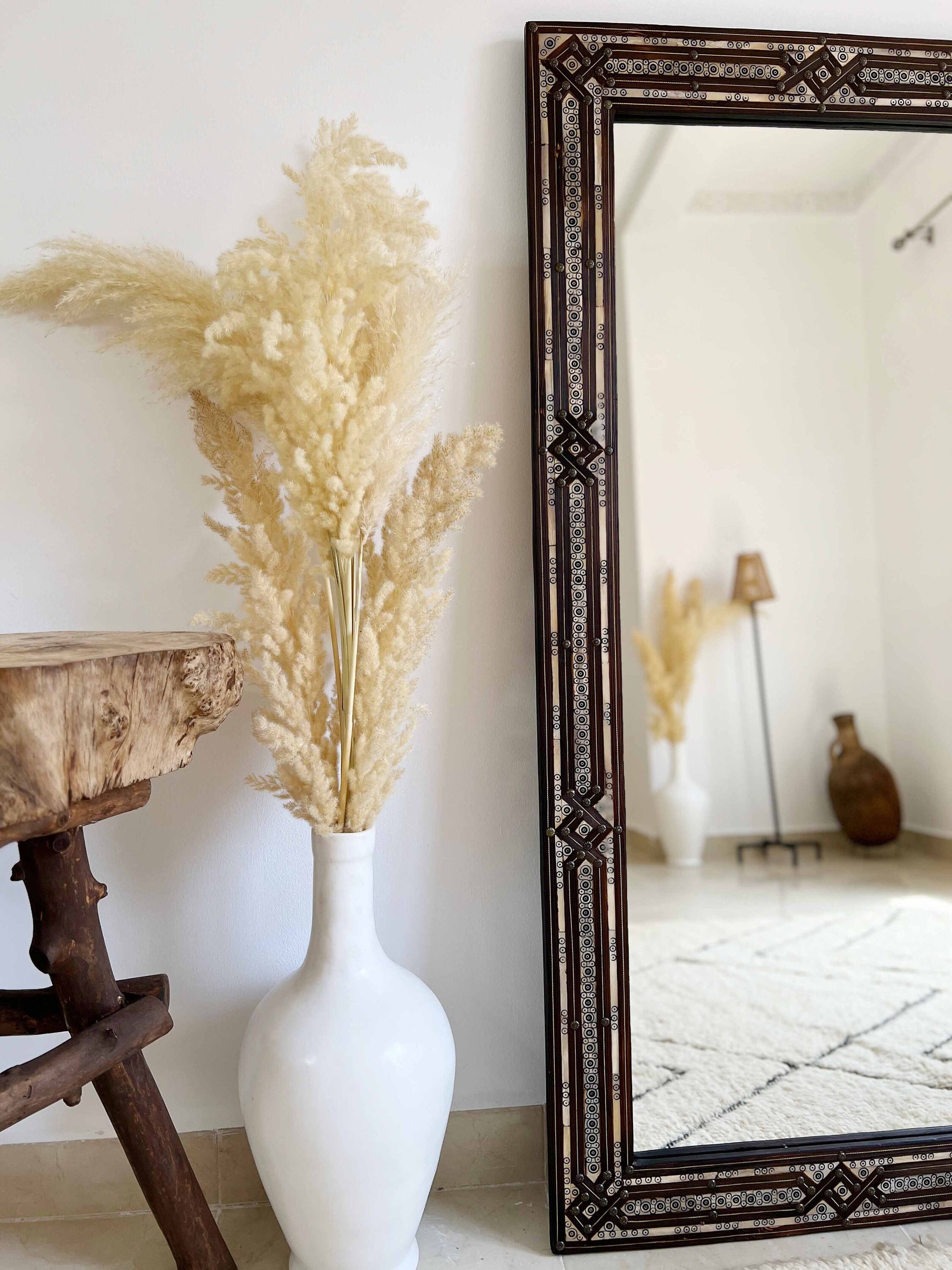 a white vase with a plant in it next to a mirror