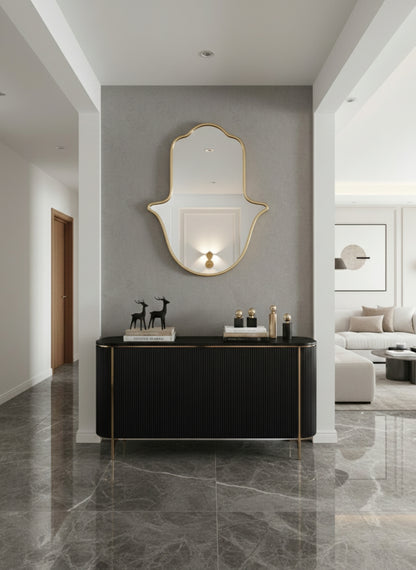 Gold Hamsa wall mirror above black console in modern entryway.