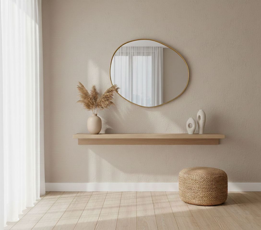 Raw edge brass mirror styled above a floating shelf in a minimalist interior