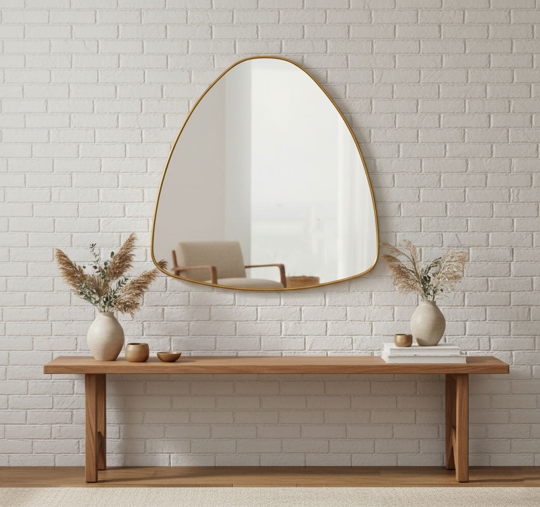 Organic triangle pebble mirror with slim brass frame on white brick wall