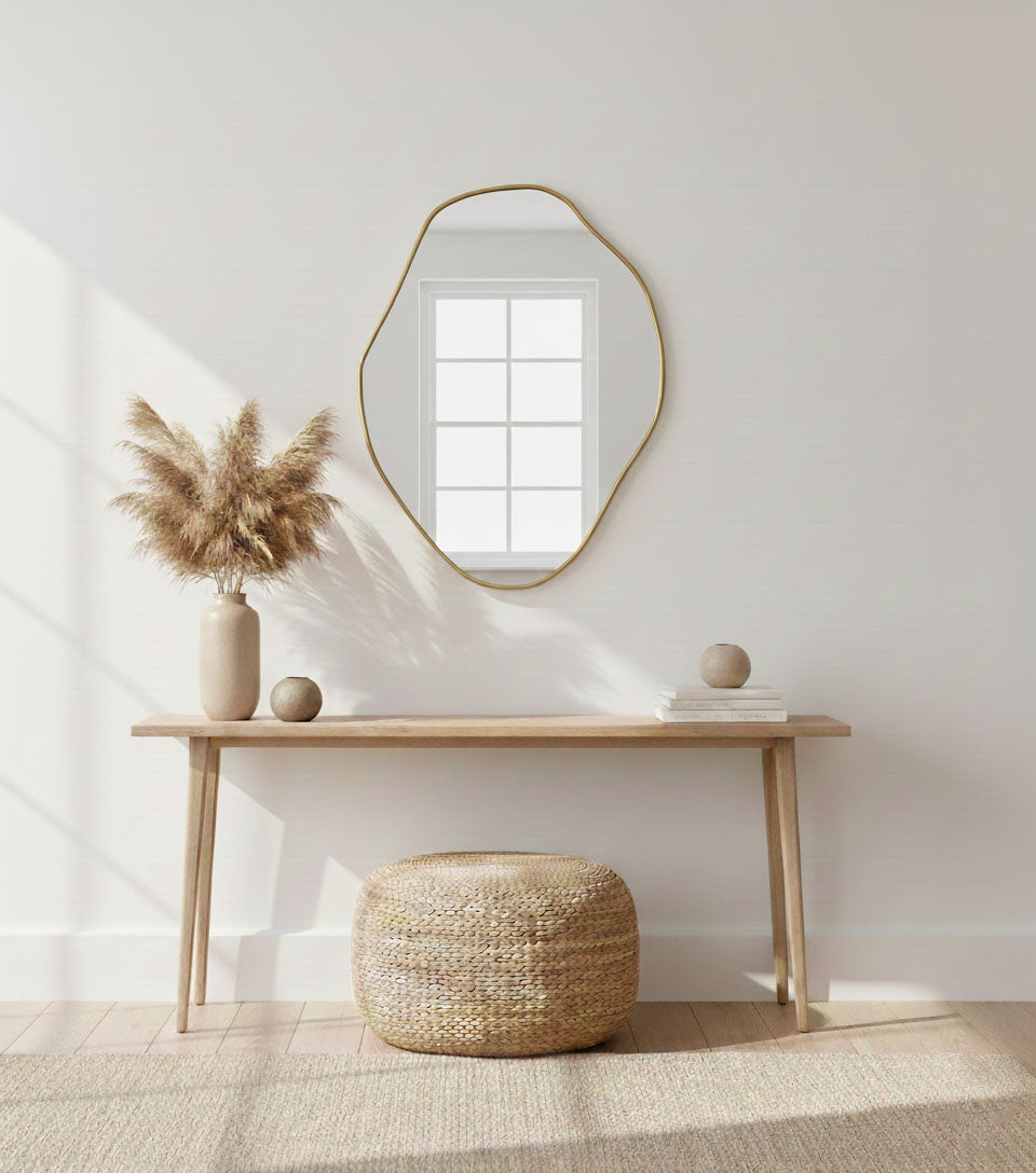 Sculptural freeform brass mirror above console table in minimalist entryway