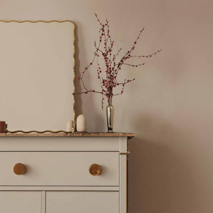 a white dresser with a Wavy Mirror and vase on top of it