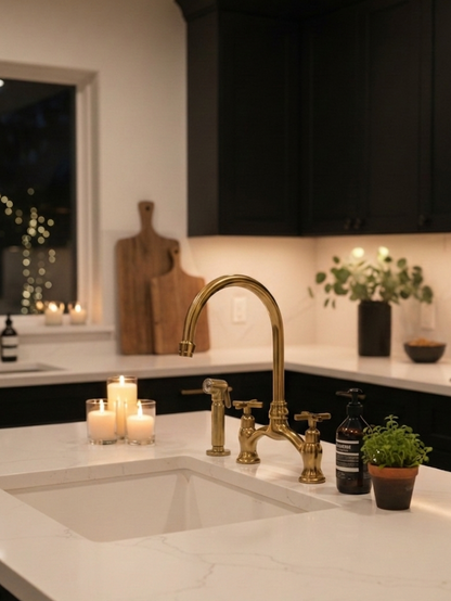 Antique brass bridge kitchen faucet with side sprayer installed beside a white farmhouse sink in a blue shaker kitchen.