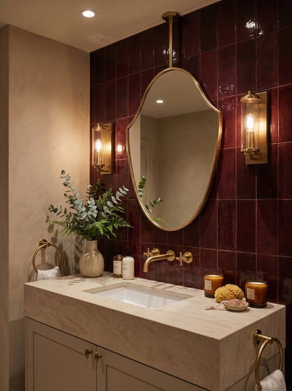 Ceiling-mounted brass shield mirror styled over a stone vanity with rich burgundy tile walls.