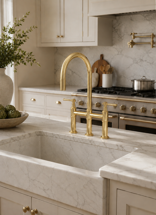 Elegant solid brass bridge kitchen faucet with pull-down sprayer mounted on a white marble farmhouse sink in a classic luxury kitchen.