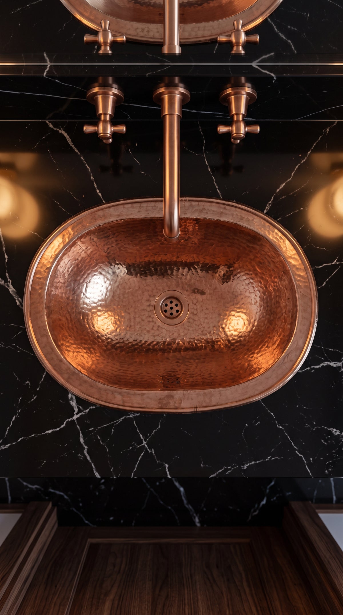 Overhead view of an oval hammered copper sink in a black marble countertop beneath a matching wall-mounted faucet.