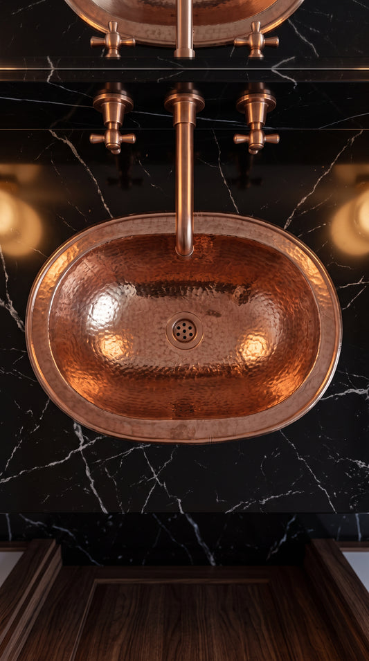 Overhead view of an oval hammered copper sink in a black marble countertop beneath a matching wall-mounted faucet.
