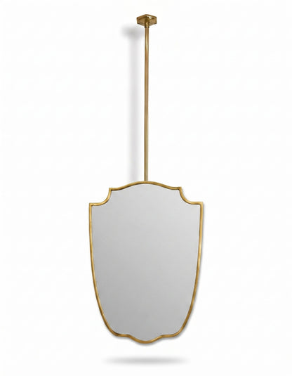 Gold framed shield mirror suspended from ceiling rod on white background