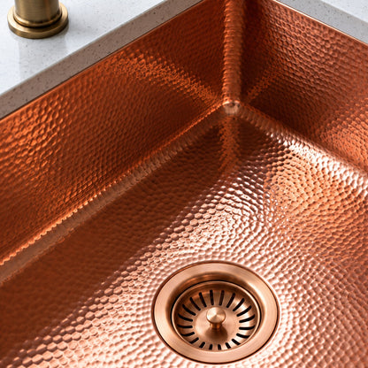 Close-up of a hammered copper basin showing its textured walls, rounded interior corner, and matching basket-strainer drain.