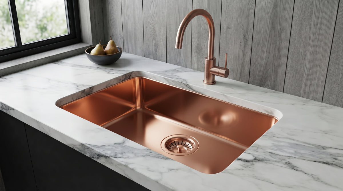 Polished copper undermount sink with matching gooseneck faucet in white marble, beside a window and gray wood wall panels.