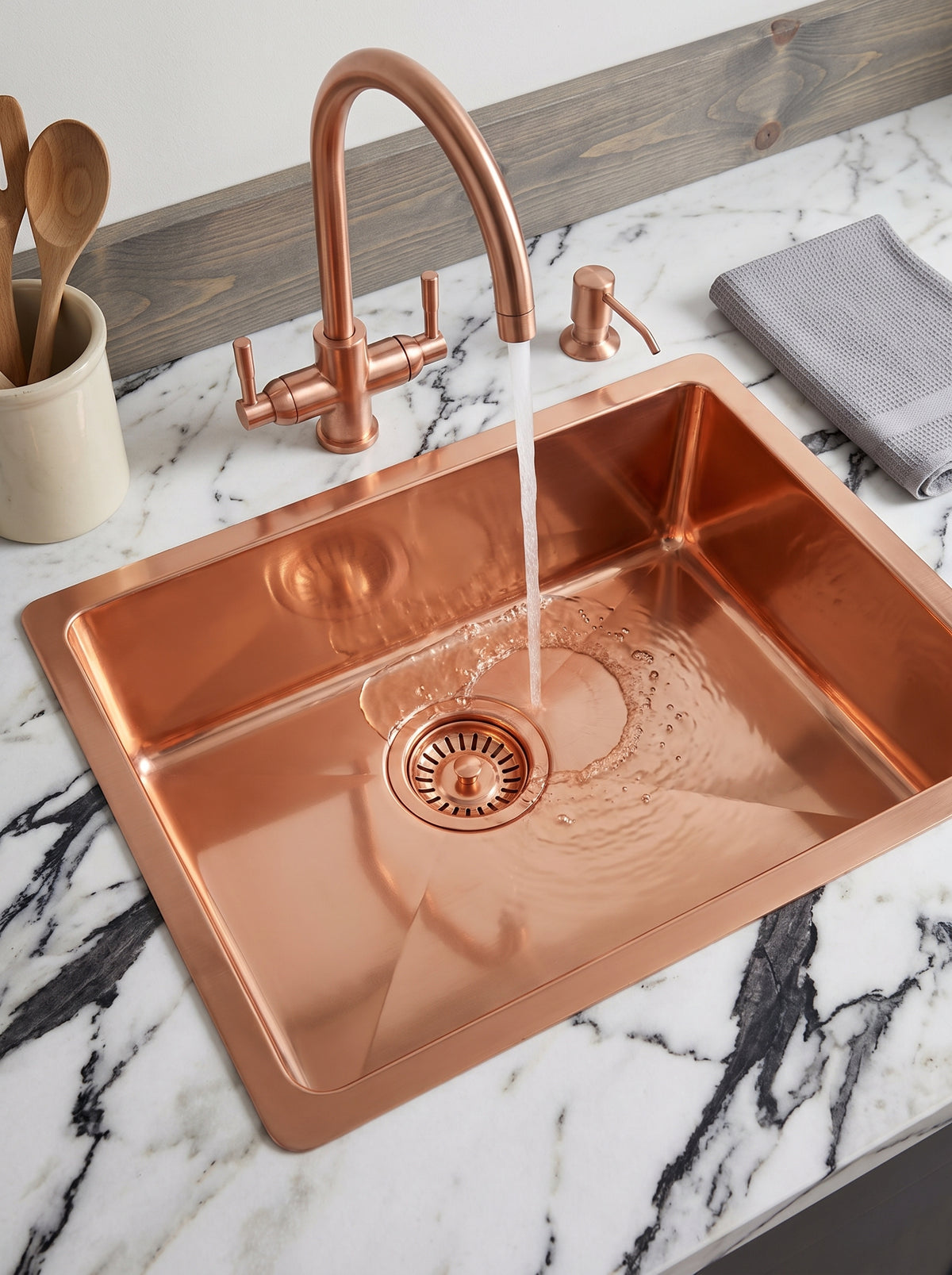 Copper kitchen sink with water flowing from a matching curved faucet, creating ripples in the basin on a white marble countertop.