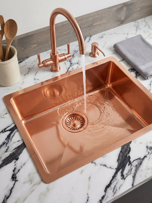 Copper kitchen sink with water flowing from a matching curved faucet, creating ripples in the basin on a white marble countertop.