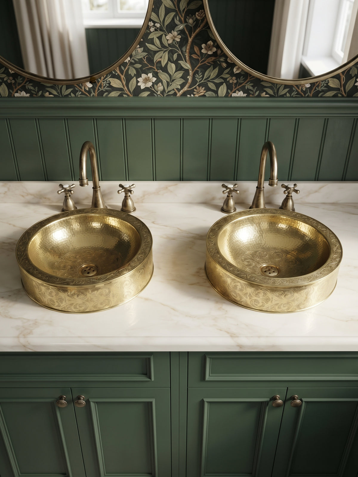 Two engraved brass vessel sinks on a white marble double vanity with green cabinets, brass faucets, and floral wallpaper.