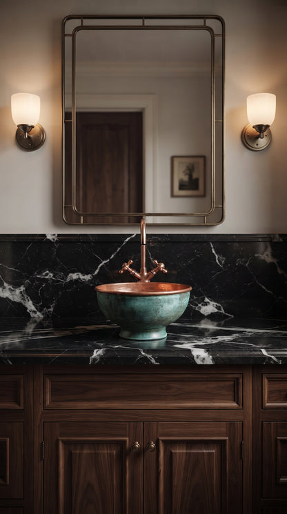 Turquoise-patina copper vessel sink with a tall copper faucet on black veined marble, beneath a rectangular mirror and two wall sconces.