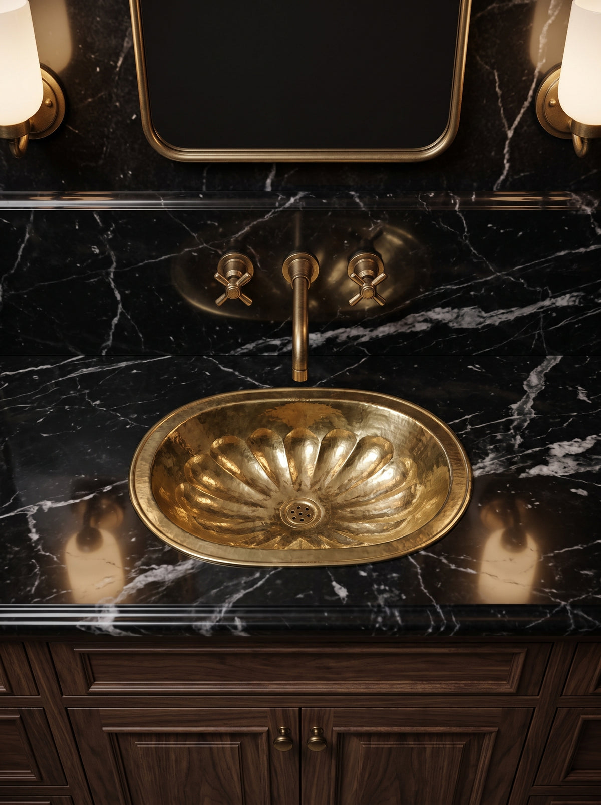 Oval brass sink with hammered flower-petal detailing in a black marble vanity with a brass wall-mounted faucet and dark wood cabinets.
