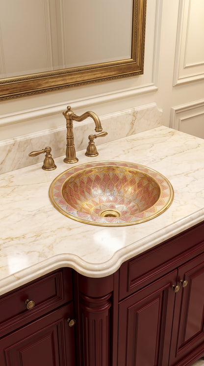 Round brass sink with copper and silver geometric patterns in a cream marble vanity with brass faucet and burgundy cabinets.