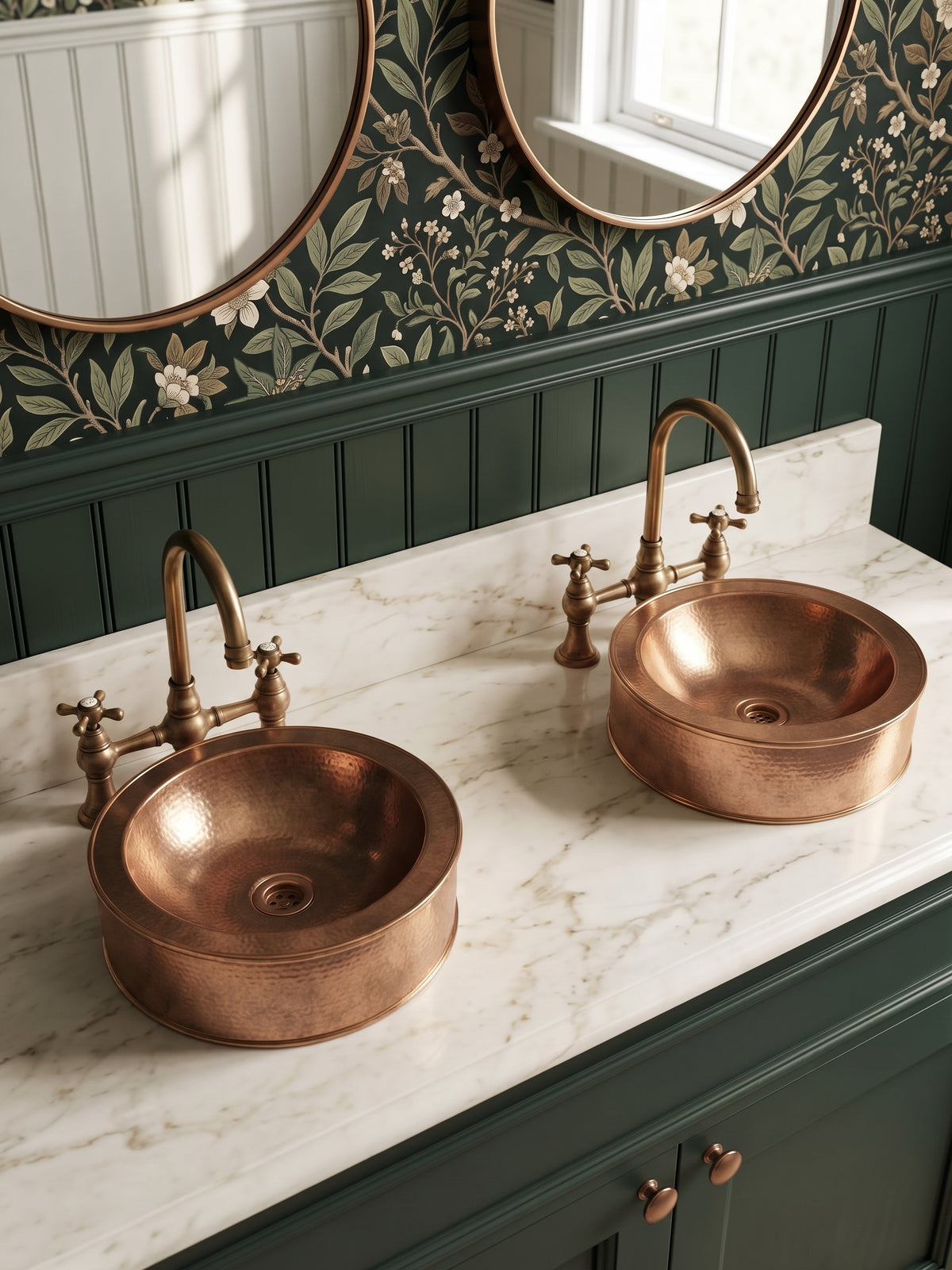 Two hammered copper vessel sinks on a white marble double vanity with brass bridge faucets, green cabinets, and floral wallpaper.