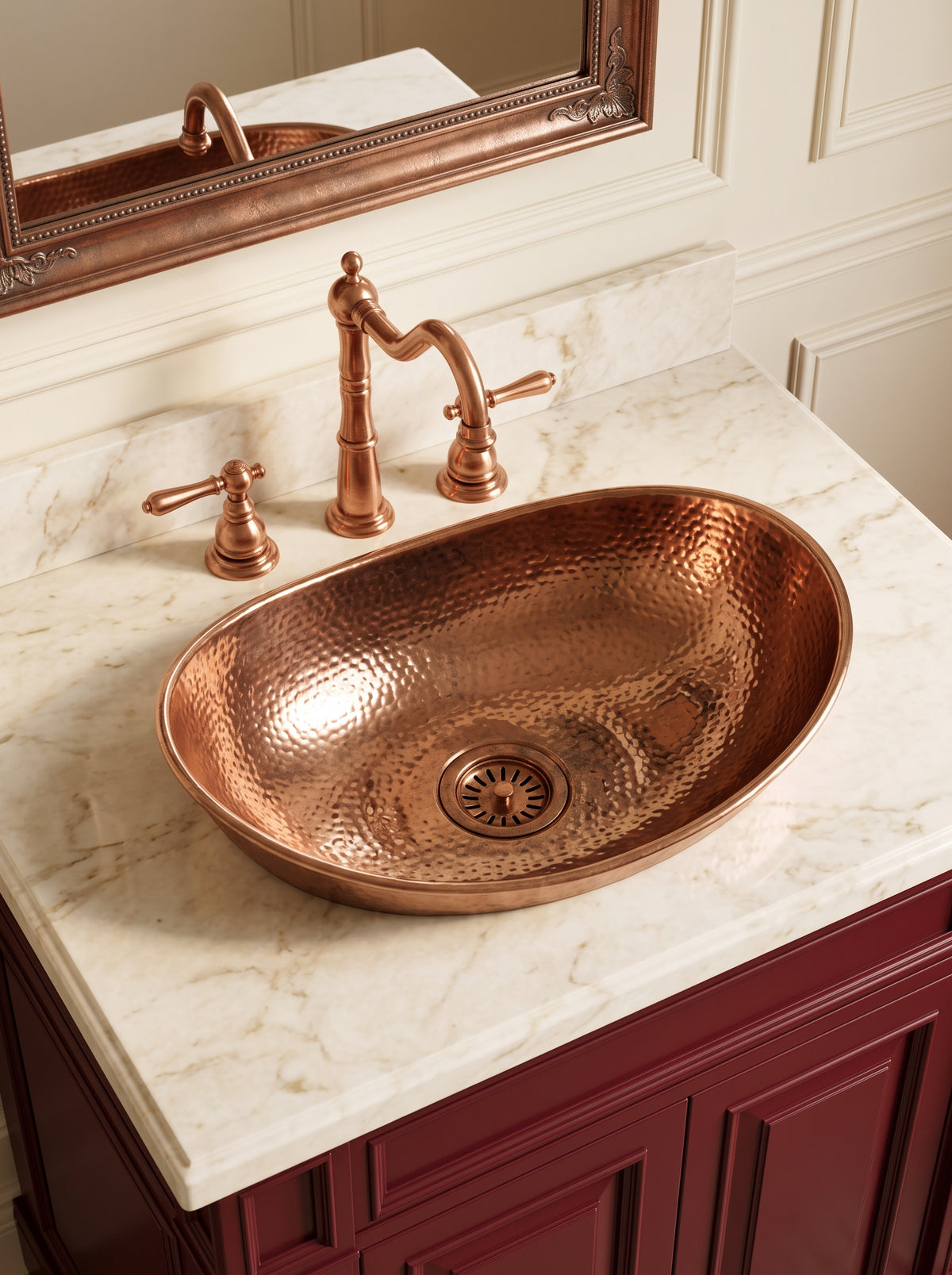 Oval hammered copper vessel sink with matching three-piece faucet on cream marble above a burgundy vanity.