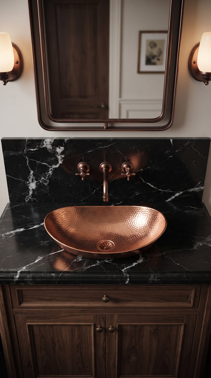 Hammered copper vessel sink on black veined marble, paired with a wall-mounted copper faucet beneath a rectangular mirror.