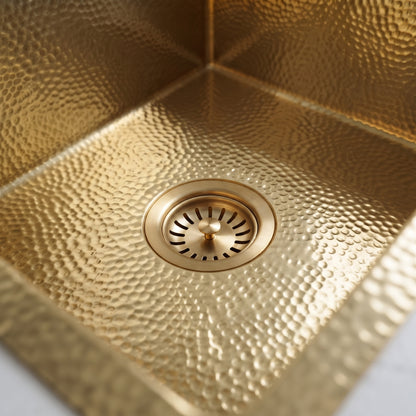 Close-up of a gold basket-strainer drain surrounded by the kitchen sink’s hammered metallic texture.