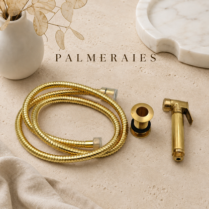 Solid brass kitchen side sprayer with matching brass hose and mounting sleeve displayed on a neutral stone surface with luxury styling accessories.