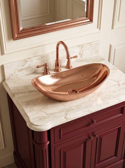 Polished oval copper vessel sink on a cream marble countertop, paired with a copper faucet above a burgundy vanity.