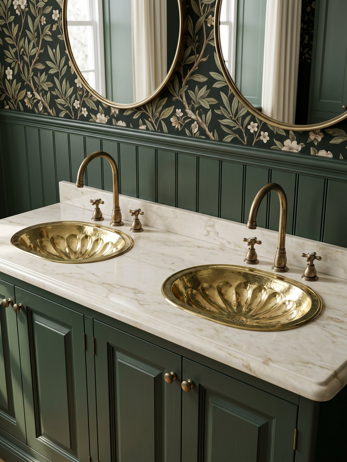 Two oval brass sinks with hammered flower-petal detailing in a white marble double vanity with green cabinets, brass faucets, and oval mirrors.