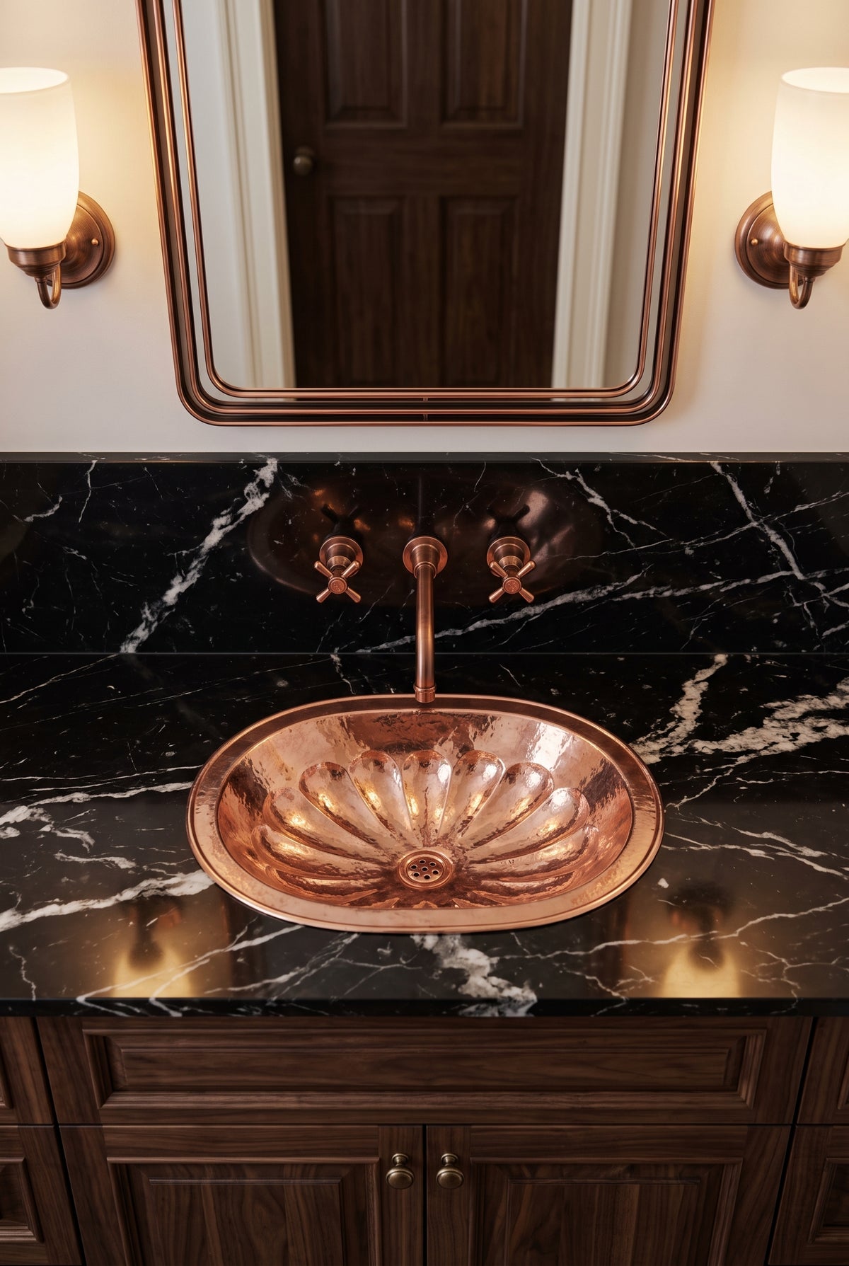 Oval copper flower-pattern sink in a black marble vanity beneath a matching wall-mounted faucet, copper-framed mirror, and sconces.