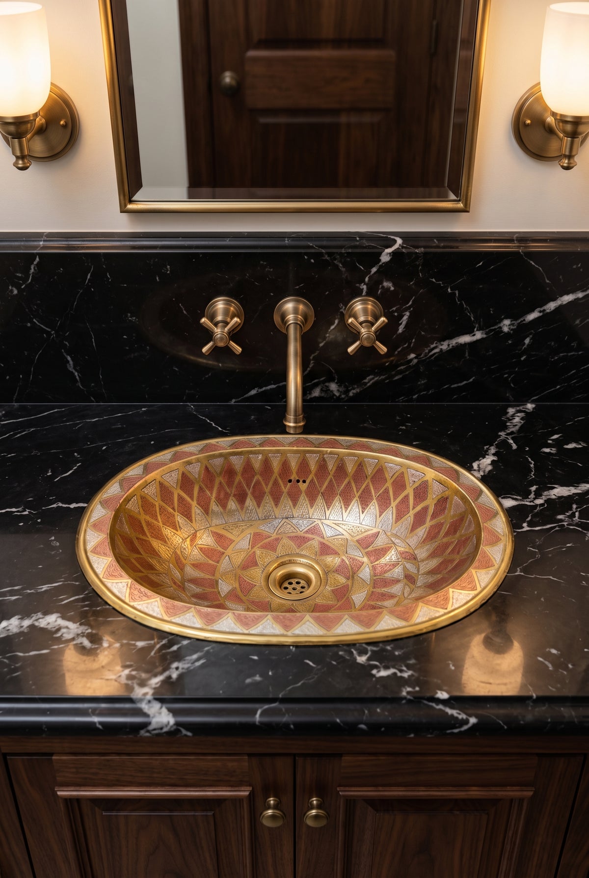 Oval sink with gold, copper, and silver geometric patterns in a black marble vanity beneath a brass wall-mounted faucet and mirror.