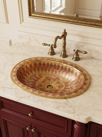 Oval geometric-patterned metal sink in a cream marble countertop with a brass faucet, burgundy vanity, and gold-framed mirror.