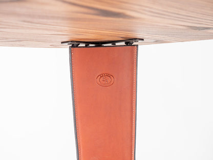Close-up of a wooden table leg with a leather strip and visible brand logo.