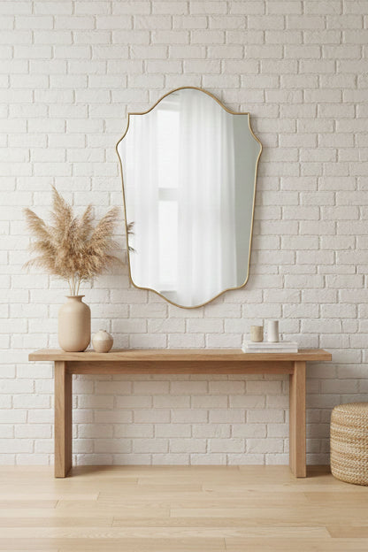 Shield brass vanity mirror styled above wooden console with neutral decor
