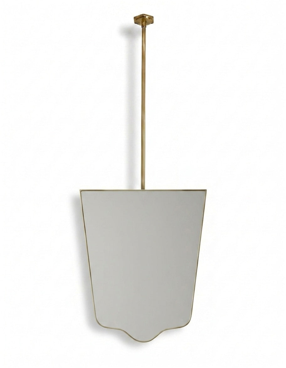 Handmade shield-shaped brass mirror with ceiling-mounted brass rod on a white background.