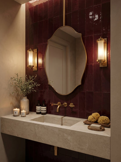 Luxury ceiling-mounted brass mirror with scalloped edges styled over a stone vanity against glossy burgundy tiles.