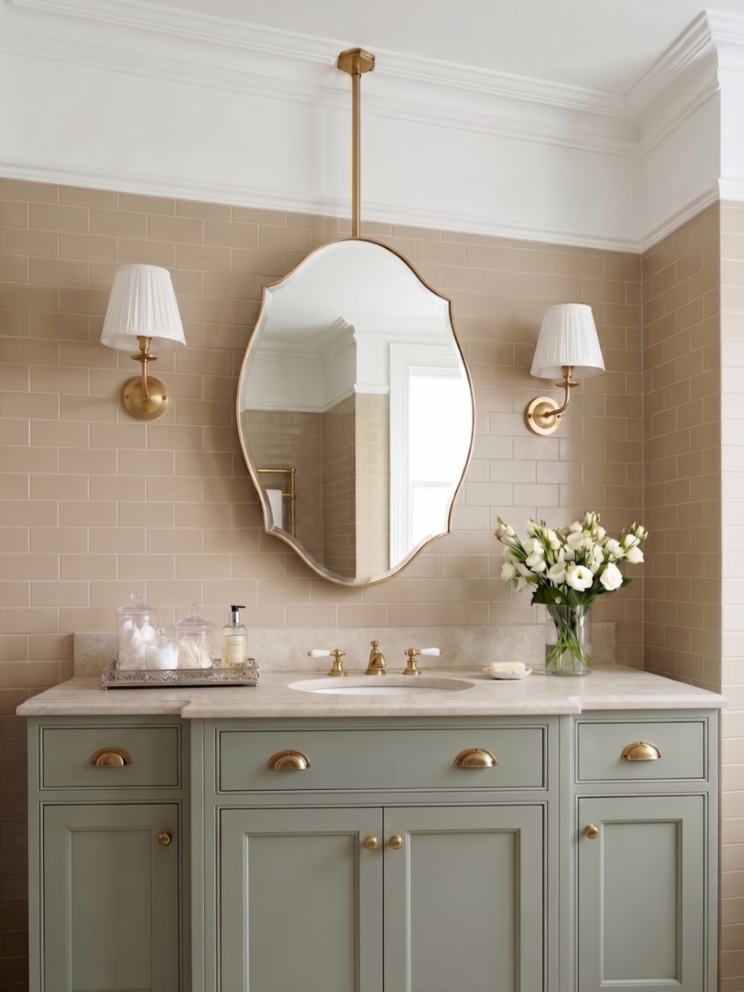 Suspended scalloped shield brass mirror above a sage green bathroom vanity with brass fixtures.