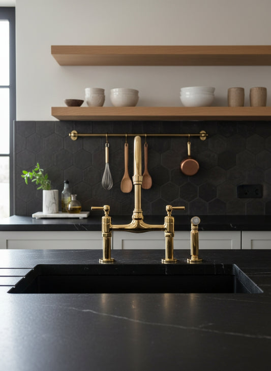 Unlacquered brass bridge kitchen faucet with side sprayer installed on a black stone countertop in a modern kitchen.