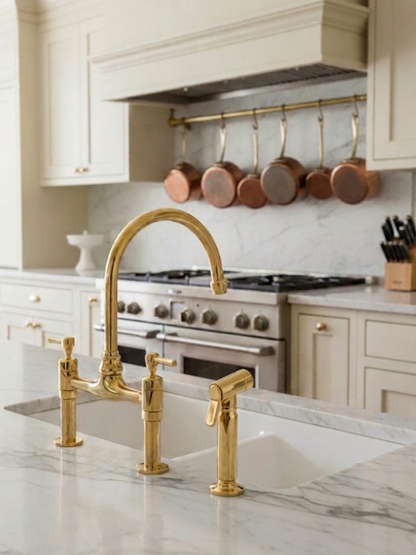 Unlacquered brass bridge kitchen faucet with side sprayer installed on a white marble countertop in a classic luxury kitchen.