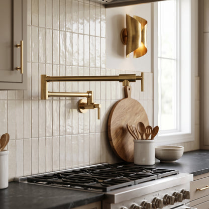 Close-up of a handmade solid brass wall-mounted pot filler faucet with articulated swing arm installed above a gas cooktop in a luxury kitchen.