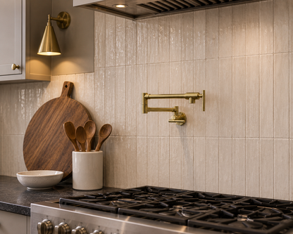 Handmade solid brass wall-mounted pot filler faucet with articulated swing arm installed above a gas cooktop in a luxury kitchen.