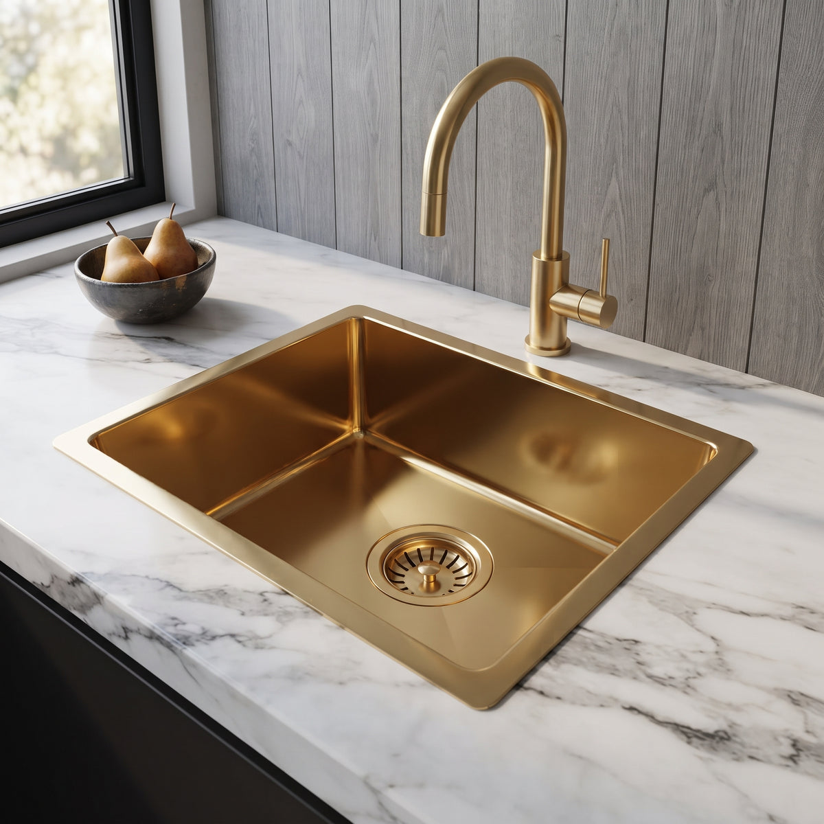 Polished brass drop-in sink with matching gooseneck faucet in a white marble countertop, beside a window and gray wood panels.