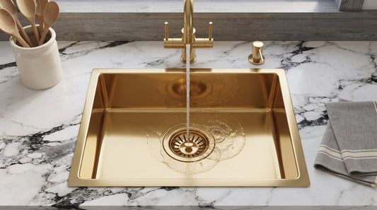 Brass drop-in sink with water flowing from a matching faucet, creating ripples around the drain on a boldly veined marble countertop.