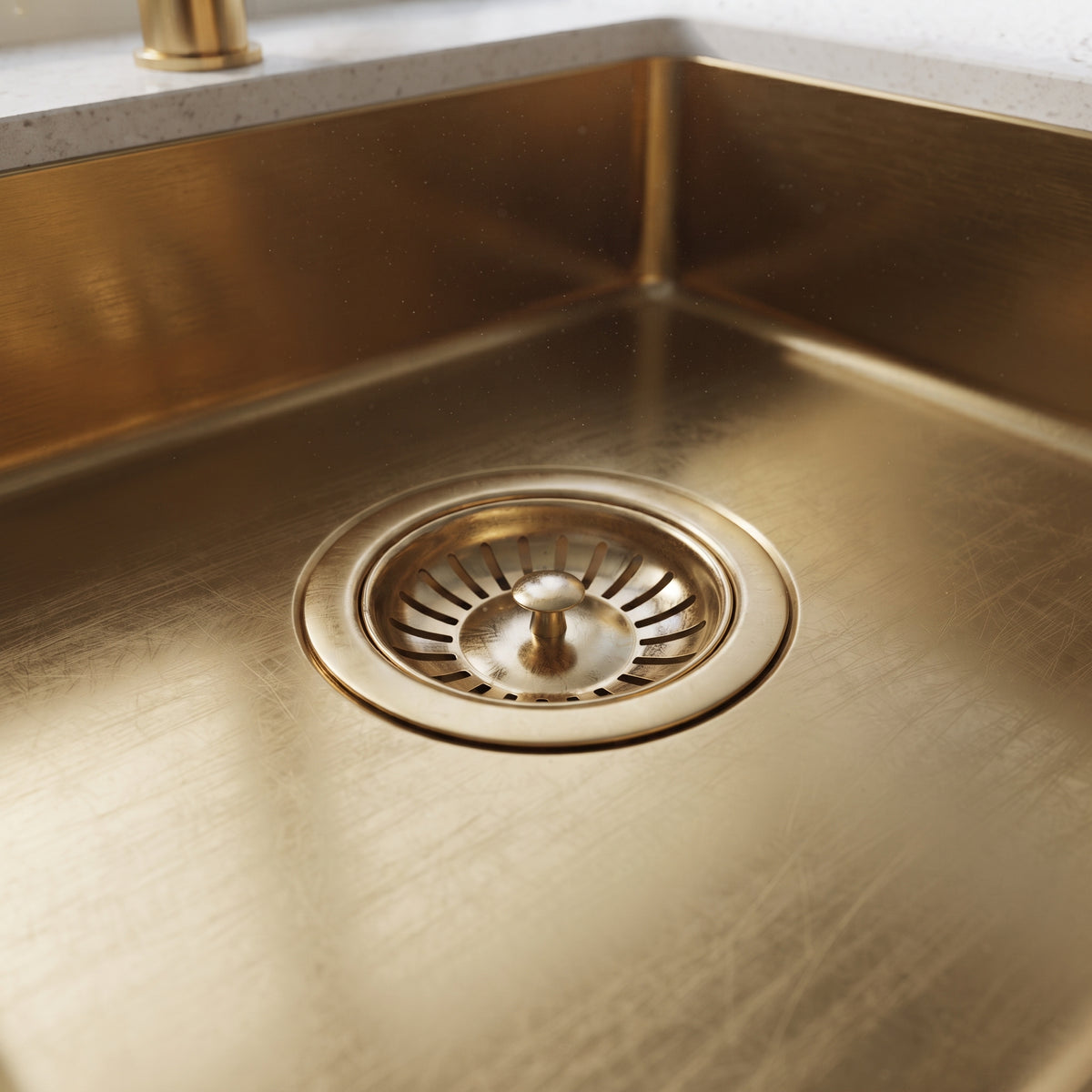 Close-up of a smooth unlacquered brass kitchen sink showing its basin, rounded interior corner, and matching basket-strainer drain.