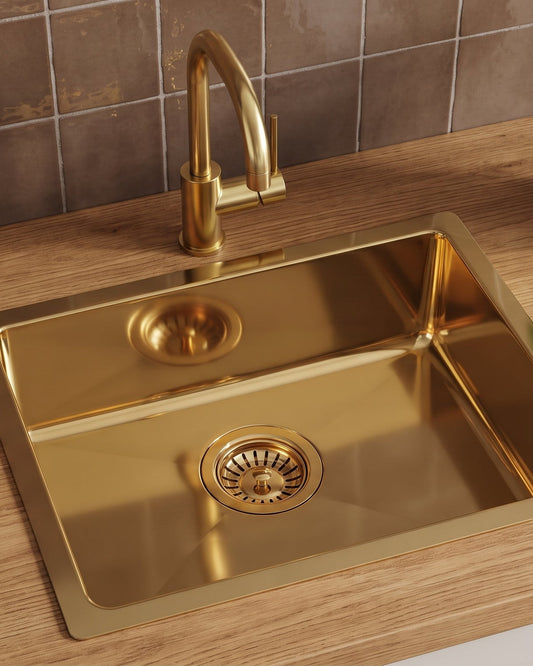 Brass drop-in sink with matching gooseneck faucet on an oak countertop, against brown tiles beside a basil plant.