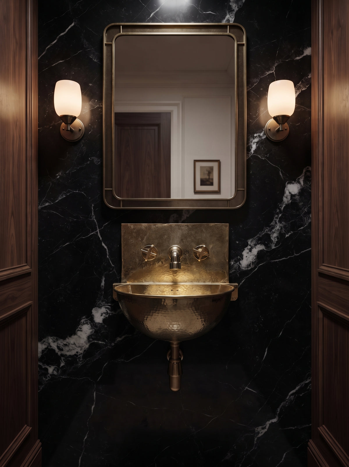 Unlacquered brass wall-mounted sink against black veined marble, beneath a rectangular mirror flanked by warm wall sconces.