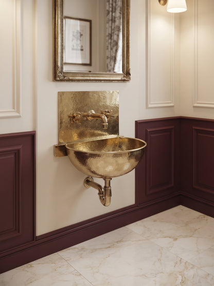 Angled view of a brass wall-mounted sink with rectangular backsplash and exposed plumbing in a cream and burgundy paneled bathroom.