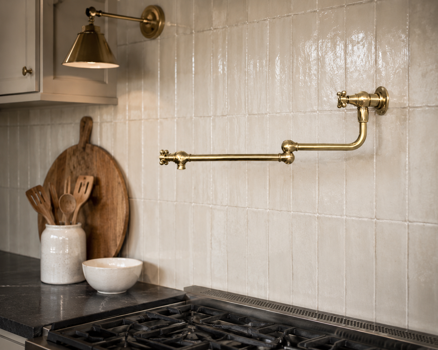 Traditional brass wall mounted pot filler faucet installed on handcrafted cream ceramic tile backsplash above cooktop.