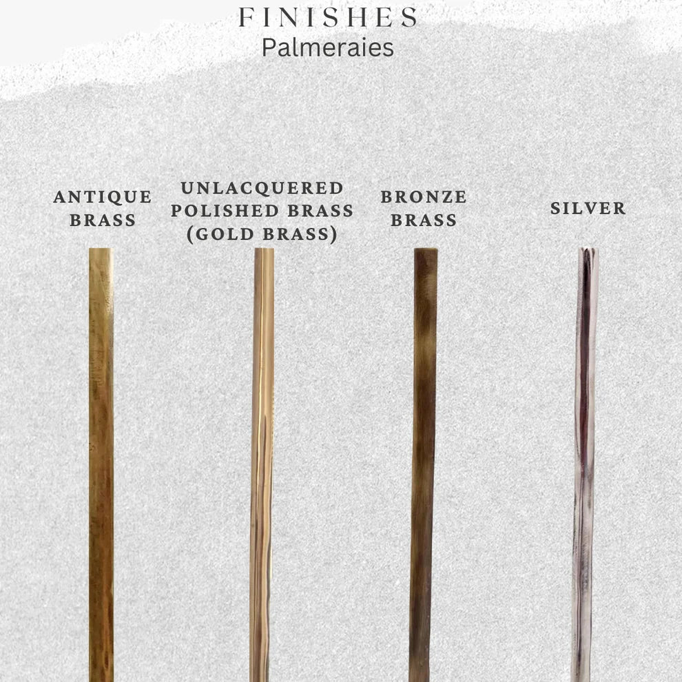 Four slender metal palmeraie stems in different finishes are displayed against a light textured background with labels: Antique Brass, Unlacquered Polished Brass (Gold Brass), Bronze Brass, and Silver.