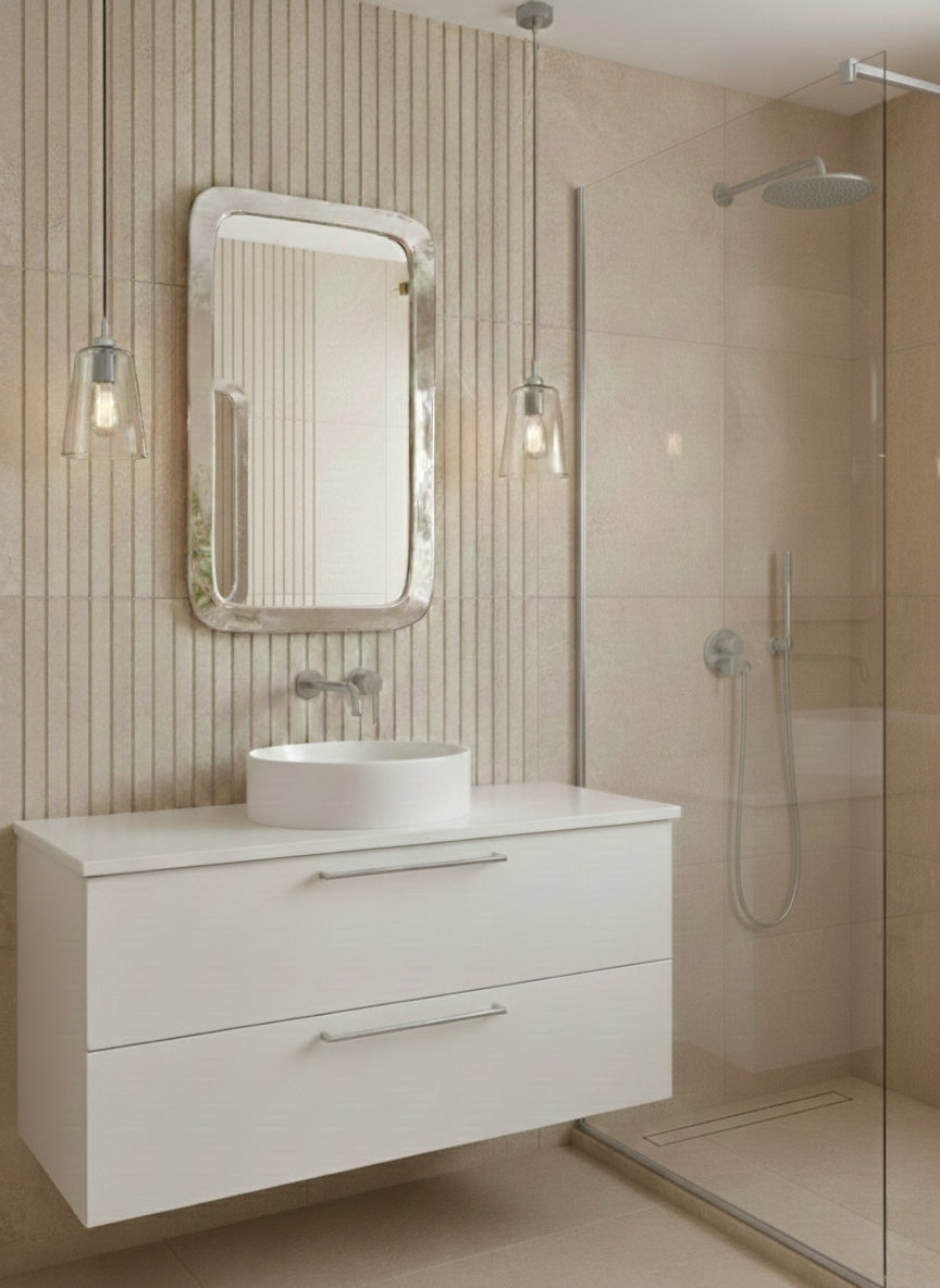Silver rounded rectangle mirror above white floating vanity in beige tiled bathroom.

